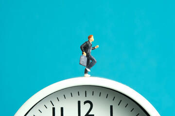 Miniature people toy figure photography. End and start of school concept. Young men pupil running above white clock isolated on blue background