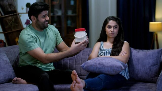 A loving husband pampering his pretty wife by giving her a wonderful gift - a surprise gift  relationship problems. A young Indian couple hugging each other while sitting on the sofa - love and aff...
