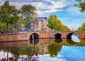 Amsterdam Downtown. Beautiful sky at sunrise, old houses, canals and bridges. Calm reflections in the water. Heart of Amsterdam.