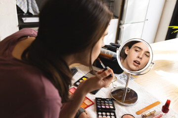 Non-binary trans woman putting lipstick looking in the makeup mirror at home