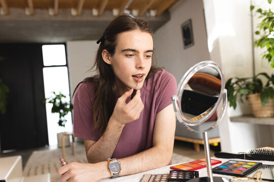 Non-binary trans woman putting lipstick looking in the makeup mirror at home
