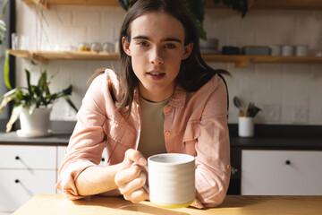 Portrait of non-binary trans woman holding a coffee cup in the kitchen at home - obrazy, fototapety, plakaty