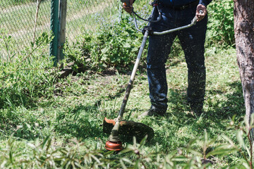 The man mowing green wild grass using brush cutter mower or power tool string lawn trimmer. To mow...