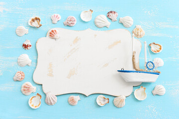 nautical concept with white sail boat, seashells and blank board for copy space over blue wooden background