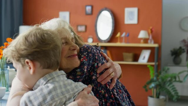 Little boy and girl hugging happy senior grandmother while gathering together for family dinner at home