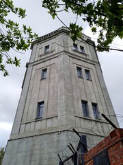 Obraz premium Vintage gray tower behind green tree leaves