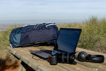 Backpack, computer, camera and headphones on a table in the wilderness - digital nomad concept