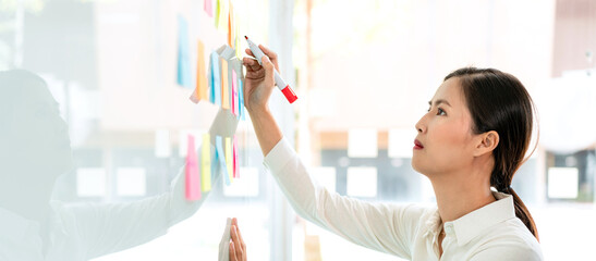 Businesswoman executive writing and taking notes keyword on board wall to planning about a new...