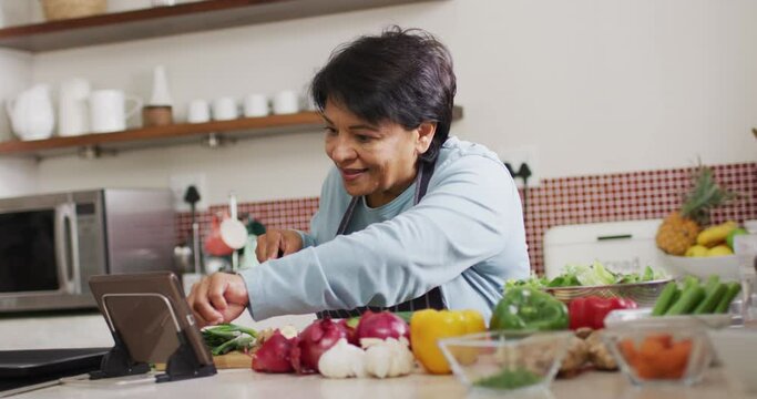 Asian senior woman using digital tablet while chopping vegetables in the kitchen at home