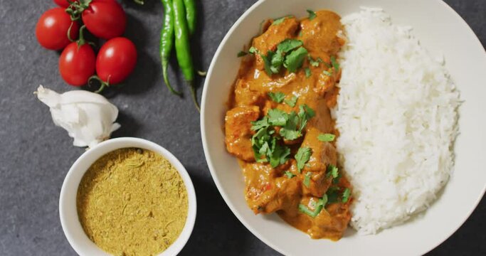 Video of plate with rice and curry, sauce and tomatoes lying in grey background