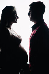 The silhouette of a man in a T-shirt and a pregnant woman in beautiful underwear on a white background. Studio photo.