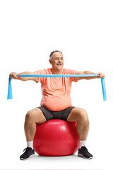 Fototapeta na wymiar Happy mature man in sportswear sitting on a fitness ball and exercising with a resistance band