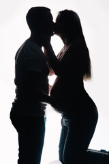 The silhouette of a man in a T-shirt and a pregnant woman in beautiful underwear on a white background. Studio photo.