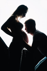 The husband kisses the pregnant wife's stomach. Dark silhouettes on a white background. Studio photo.