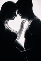 The silhouette of a man in a T-shirt and a pregnant woman in beautiful underwear on a white background. Studio photo.