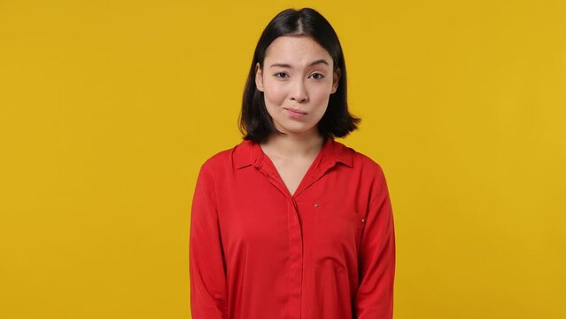 Secret fun young woman of Asian ethnicity 20s wears red shirt look aside say hush be quiet with finger on lips shhh gesture isolated on plain yellow background studio portrait. People emotions concept
