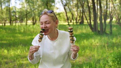 Mature woman 50 years old eating grilled vegetables from wooden skewers outdoors
