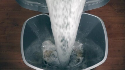 Slow motion - Soapy water being tipped into a dirty plastic trash can.