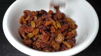 Slow motion - Brown seedless raisins pouring into a white bowl.