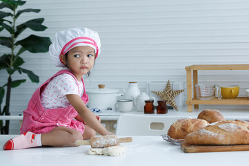 Cute little chef sitting on the table learning to make bread