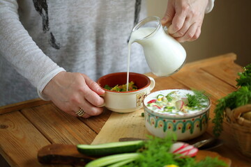 Women's hands pour kefir into okroshka