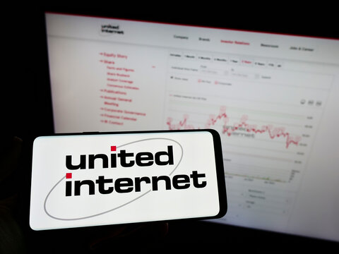 Stuttgart, Germany - 05-21-2022: Person holding mobile phone with logo of German company United Internet AG on screen in front of business web page. Focus on phone display.