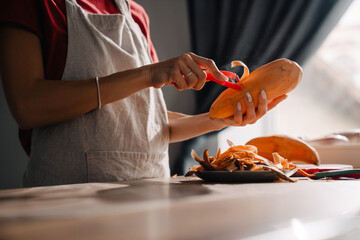 Young woman wearing apron peeling sweet potato while cooking in kitchen