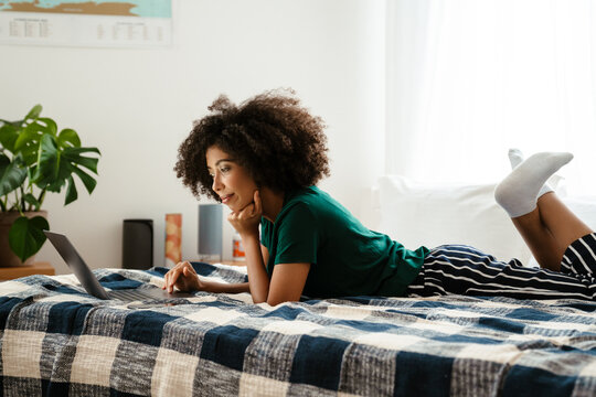 African american young woman lying in bed and using laptop at home