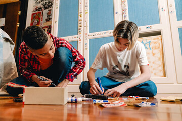 Two young teenagers sitting on floor and doing name tags in bedroom