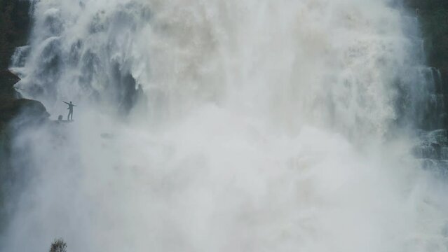 A tiny silhouette of a person under the overflowing raging Tvinderfossen waterfall. Slow-motion