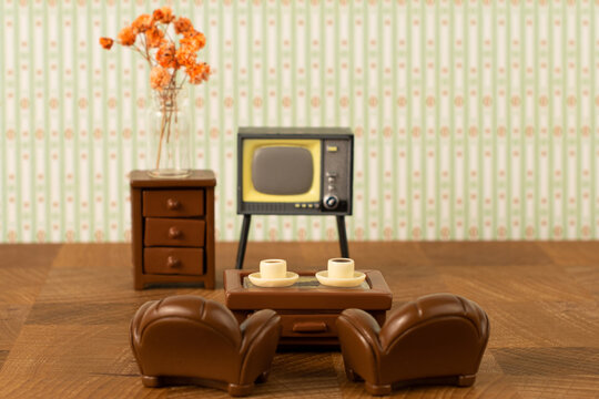 Miniature toy leather armchairs stand in front of the TV and cups of coffee