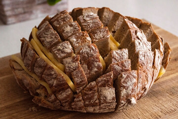 Bread and cheese snack in process of preparing. Quick snack concept. Loaf of rye bread cut in square pieces on wooden chopping board