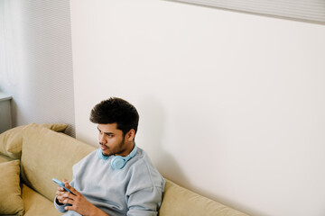 Fototapeta premium Young indian boring man with headphones on his neck
