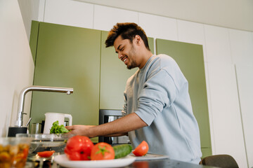 Adult indian smiling happy man washing vegetables to cook salad