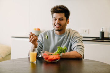 Young indian smiling man eating fresh salad