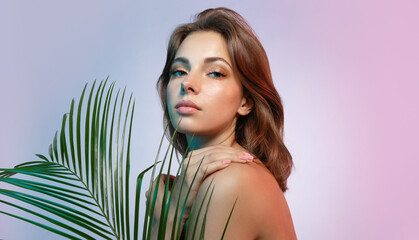 Beautiful young woman with moisturized clear skin with tropical plants on a colored background in...