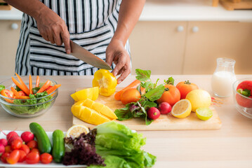 Vegetables and fruits such as mangos, lemons, bell peppers, tomatoes, carrots are prepared on the table and on a cutting board to cut, for salads in the kitchen.