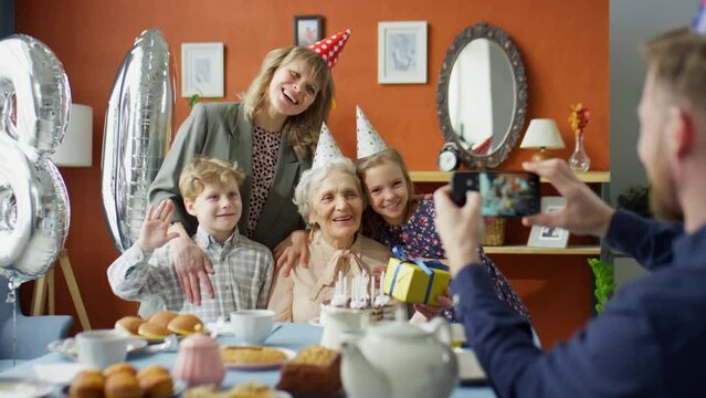 Man taking picture with smartphone of happy family and grandmother on her birthday dinner party at home