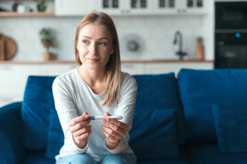 Thoughtful woman holding test when sitting on sofa