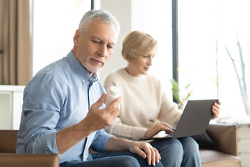 Retirement man reading label on pills while his wife checking remedy online