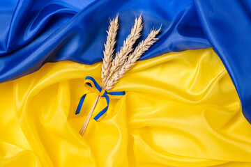 Bundle of wheat spikes with yellow and blue ribbon on Ukrainian flag background. Concept of food...
