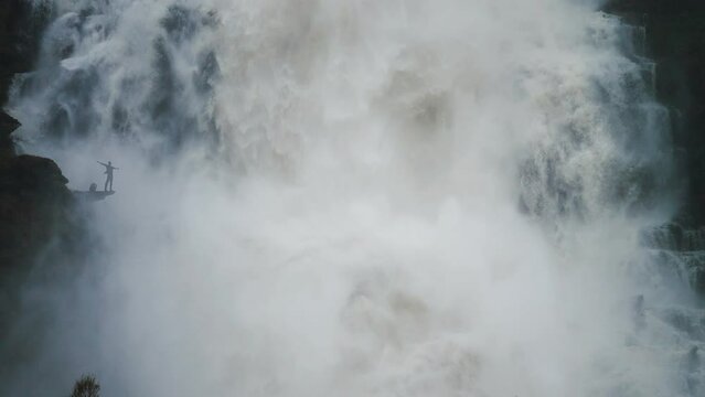 A tiny silhouette of a person under the huge raging Tvinderfossen waterfall. Slow-motion