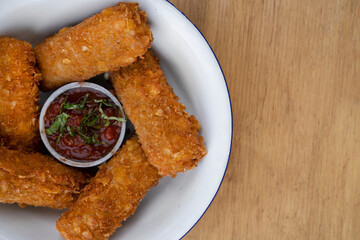 Gastronomy. Top view of fried mozzarella cheese fingers with a spicy dipping sauce, in a white bowl on the wooden table.