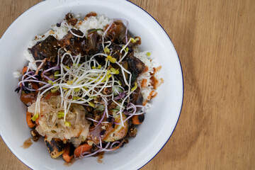 Vegan cuisine. Gluten free. Closeup view of a bowl with grilled tofu, soy sprouts, pumpkin seeds, season vegetables, spicy mango, sushi rice, cucumber and kimchi.