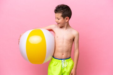 Little caucasian boy holding a beach ball isolated on pink background with happy expression