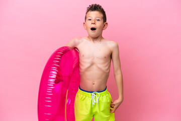 Little caucasian boy holding a inflatable donut isolated on pink background with surprise facial expression