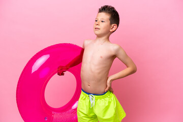 Little caucasian boy holding a inflatable donut isolated on pink background suffering from backache...