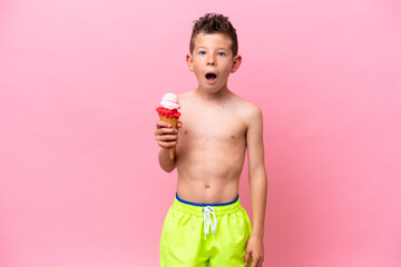 Little caucasian boy eating an ice-cream isolated on pink background with surprise and shocked...