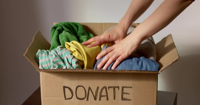 A woman volunteer puts humanitarian clothes in a box with a donation or charity. Recycling concept. Social help.