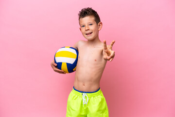 Little caucasian boy playing volleyball isolated on pink background smiling and showing victory sign